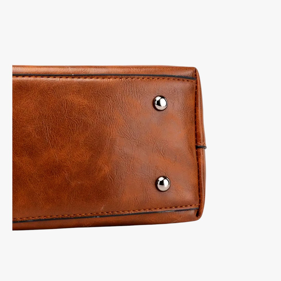 Sac à main en cuir marron avec rivets métalliques argentés sur le fond, design élégant et moderne, accessoire mode femme, vue de détail.