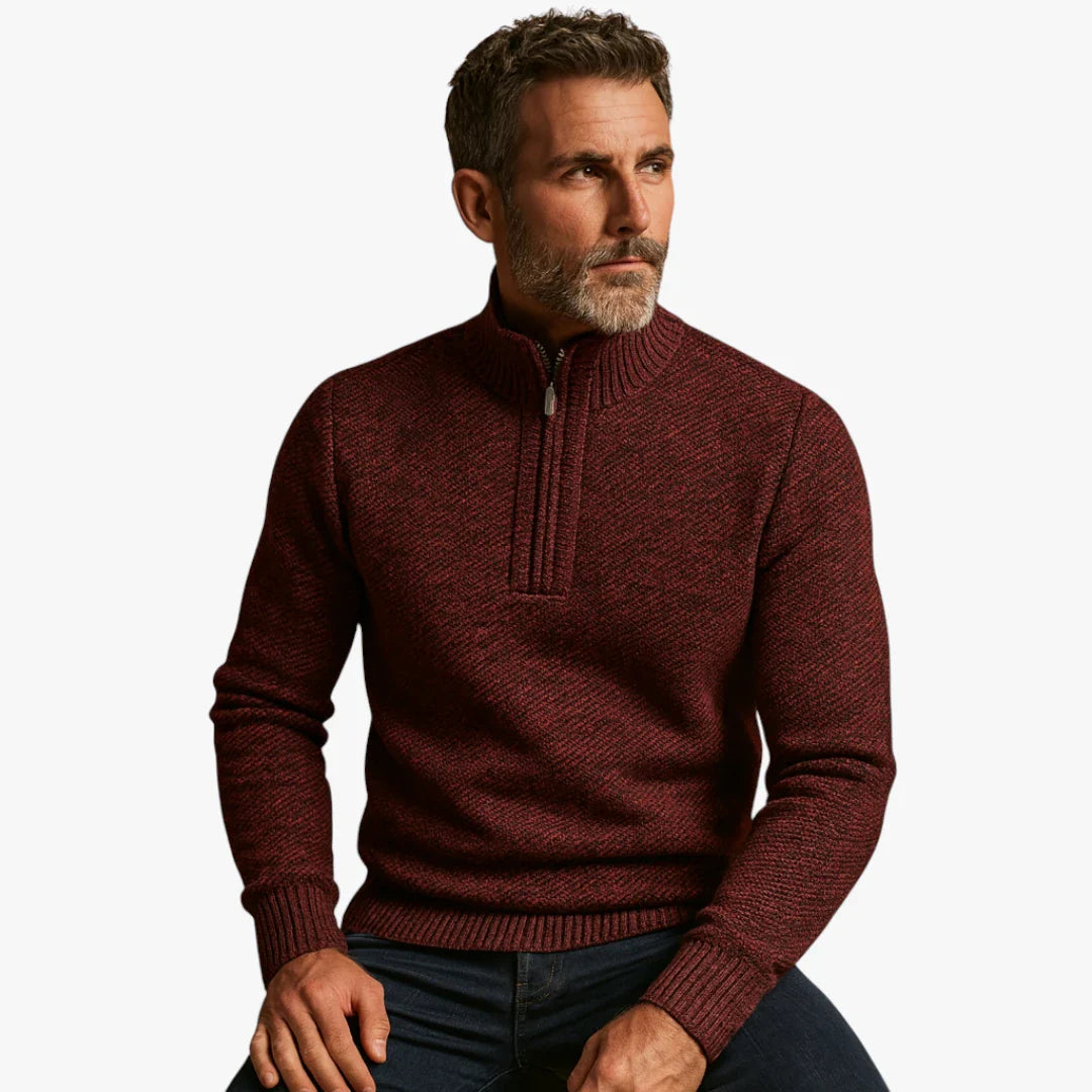 Homme portant un pull bordeaux à col zippé, assis, regard pensif. Mode masculine élégante, tenue automne-hiver, style décontracté chic.