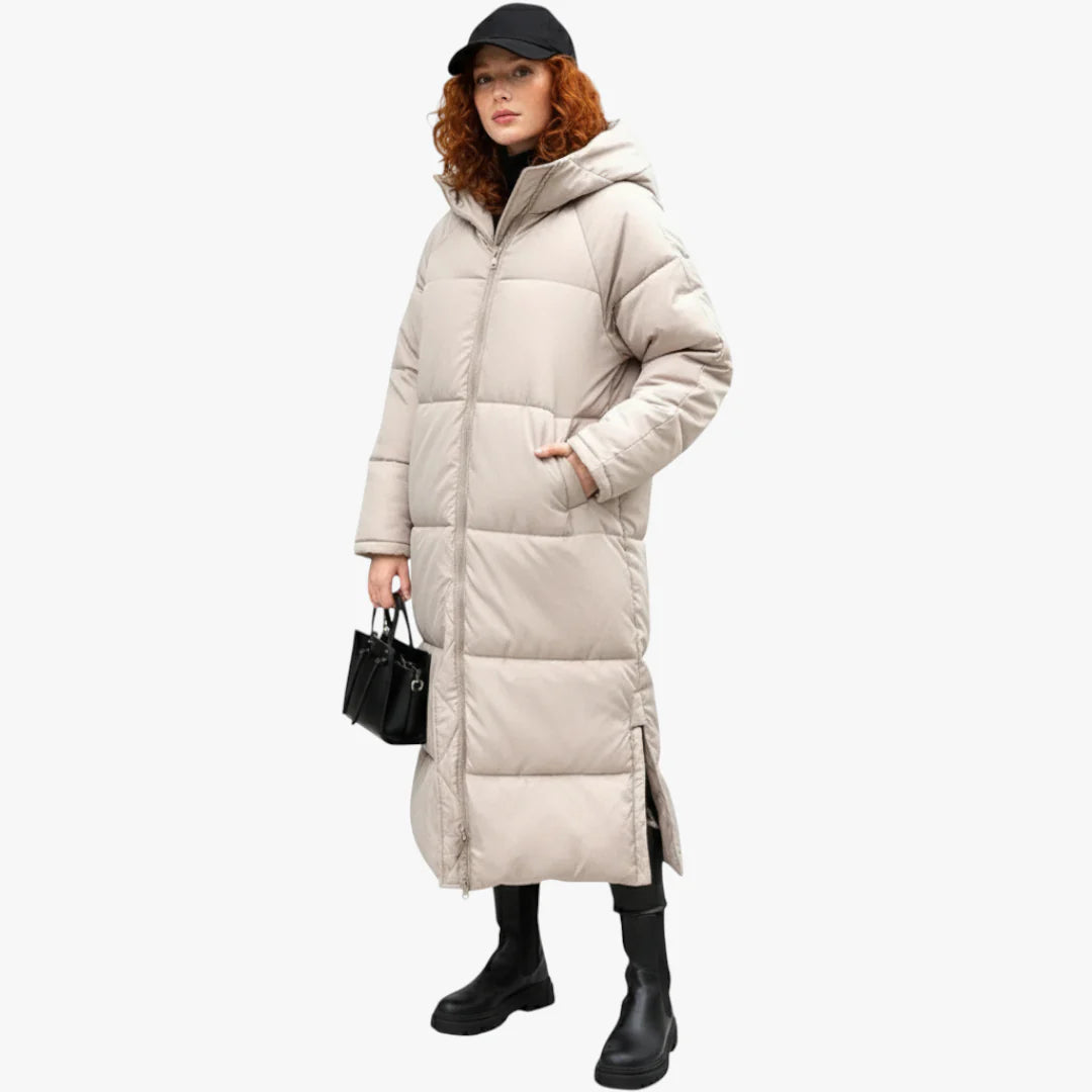 Femme portant un long manteau matelassé beige, avec capuche, tenant un sac noir. Mode hiver, style urbain, tendance vêtements chauds.