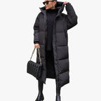 Femme portant un long manteau doudoune noir, tenue hivernale élégante, avec sac à main matelassé noir et bottes, mode tendance hiver.