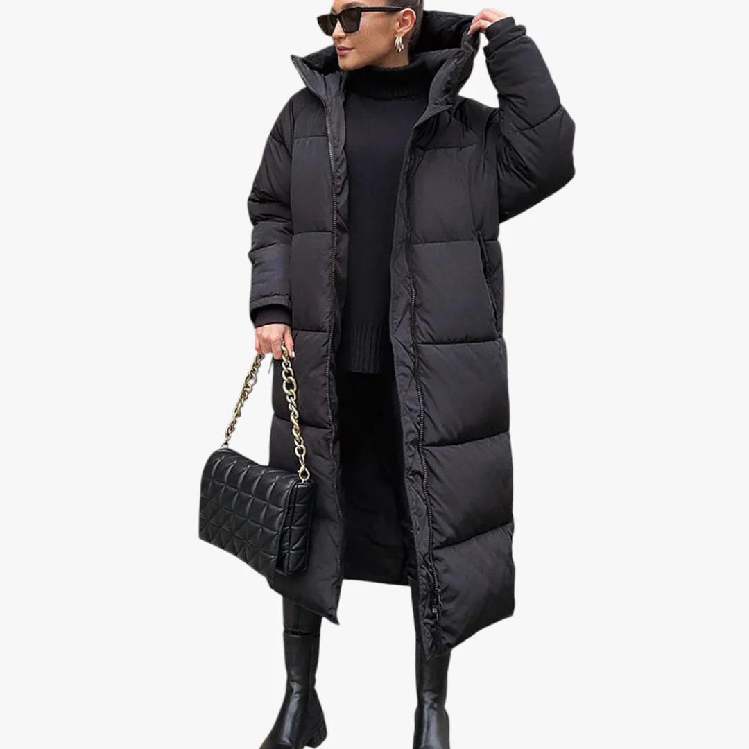 Femme portant un long manteau doudoune noir, tenue hivernale élégante, avec sac à main matelassé noir et bottes, mode tendance hiver.