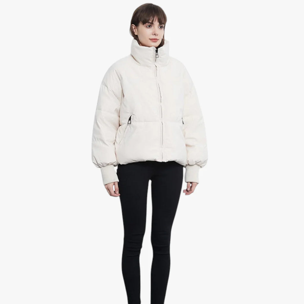 Femme portant une doudoune blanche épaisse, manches longues, col montant, fermée par une fermeture éclair, sur fond blanc. Mode hiver tendance.