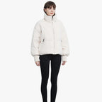 Femme portant une doudoune blanche épaisse, manches longues, col montant, fermée par une fermeture éclair, sur fond blanc. Mode hiver tendance.