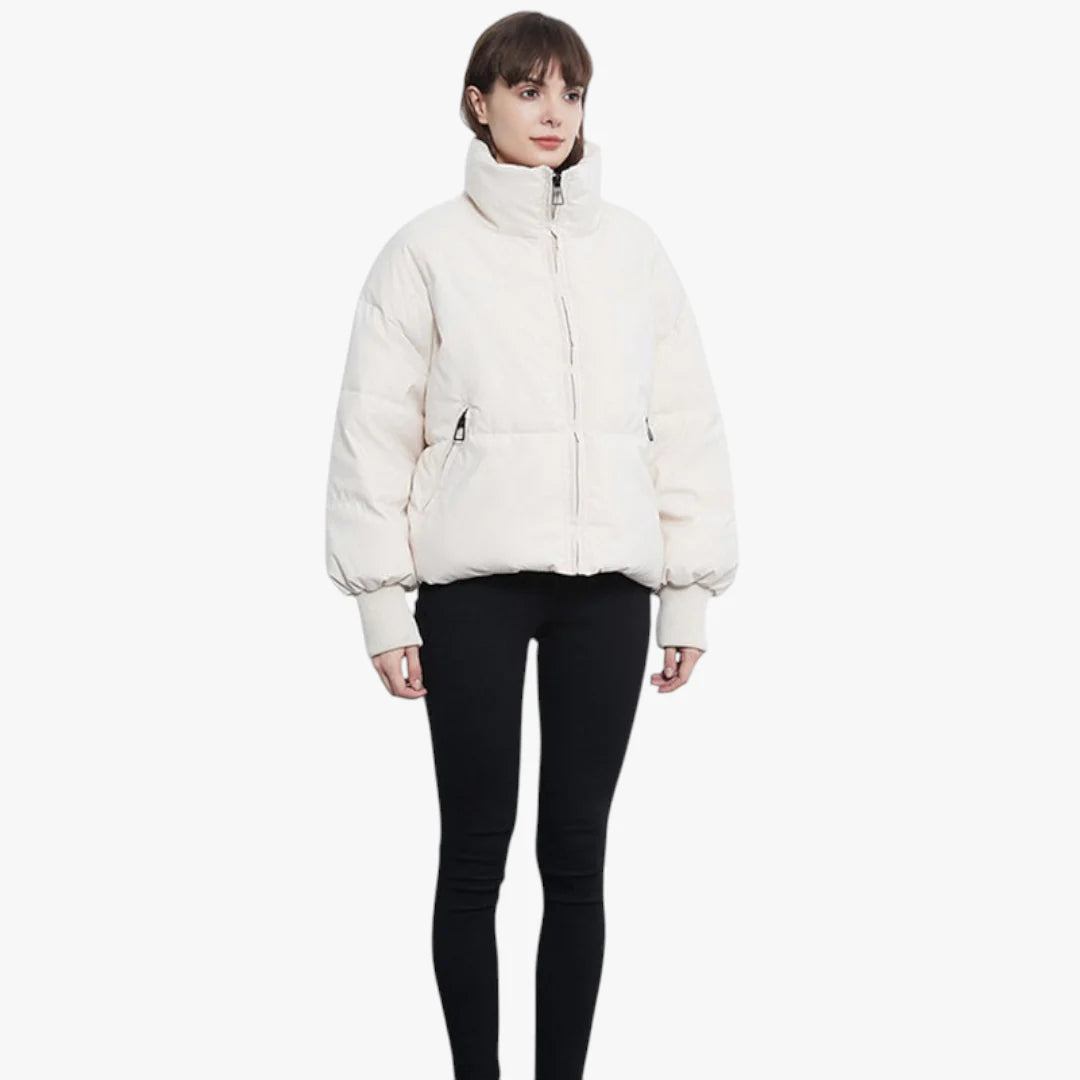 Femme portant une doudoune blanche épaisse, manches longues, col montant, fermée par une fermeture éclair, sur fond blanc. Mode hiver tendance.