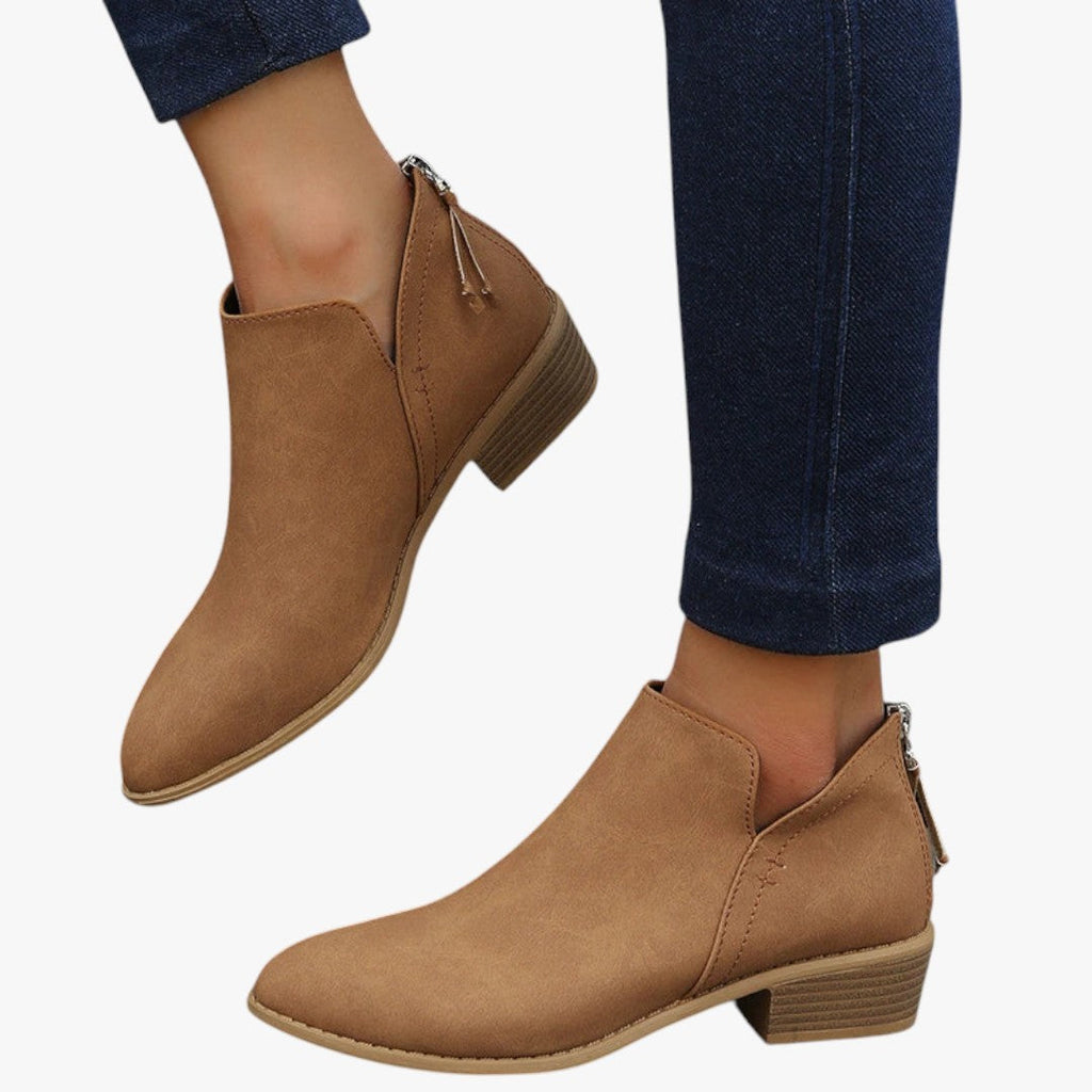 Bottines en cuir marron pour femme, talon bas, fermeture éclair arrière, portées avec un jean bleu foncé. Chaussures tendance automne-hiver.