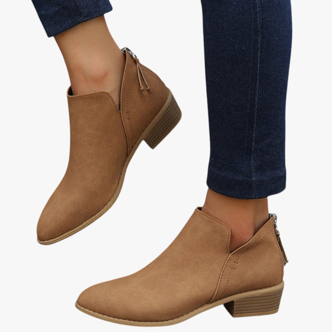 Bottines en cuir marron pour femme, talon bas, fermeture éclair arrière, portées avec un jean bleu foncé. Chaussures tendance automne-hiver.