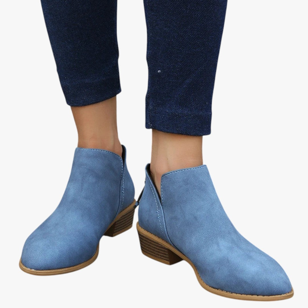 Bottines bleues en daim pour femme, talon bas, portées avec un jean foncé. Chaussures élégantes et confortables, tendance automne-hiver.