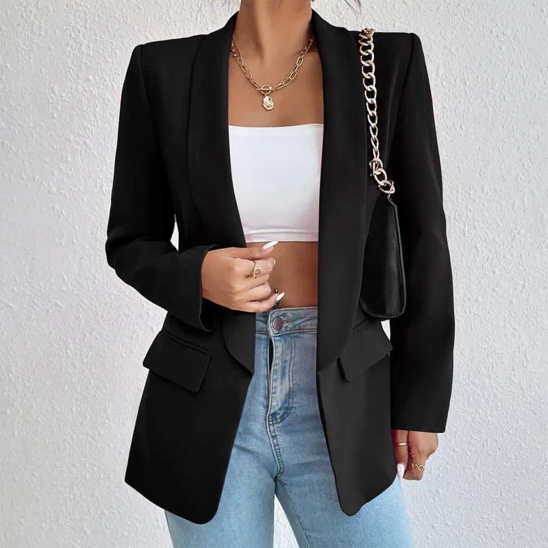 Femme portant un blazer noir élégant, top blanc, jean bleu et sac à chaîne dorée. Mode chic, tenue décontractée, style moderne.