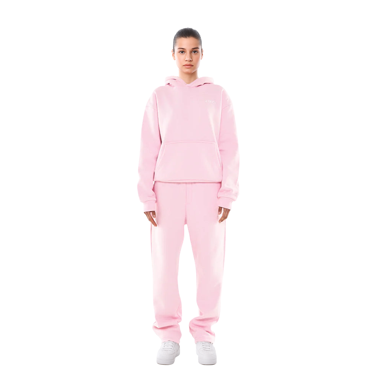 Femme portant un ensemble de survêtement rose, composé d'un sweat à capuche et d'un pantalon, sur fond blanc. Mode décontractée, tendance streetwear.