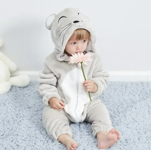Un bébé en grenouillère grise à capuche d'animal, assis sur un tapis bleu, tenant une fleur rose. Pyjama enfant, tenue mignonne, confort.