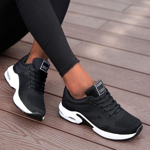 Chaussures de sport noires pour femme sur terrasse en bois, design moderne et confortable, idéales pour la marche et le fitness.