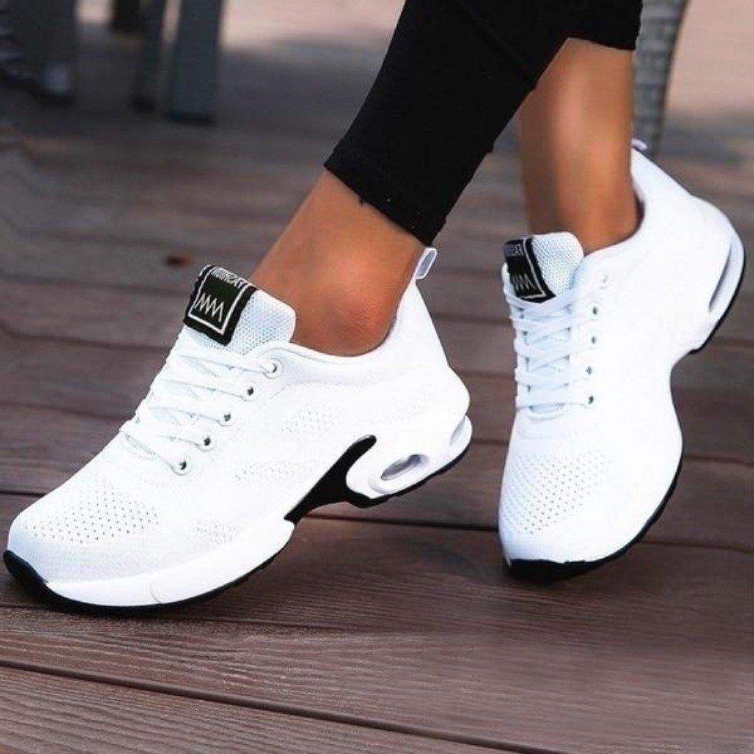 Chaussures de sport blanches pour femme, semelle épaisse, design moderne, idéales pour la course et le fitness, portées sur un sol en bois.