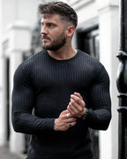 Homme musclé portant un pull noir ajusté, posant à l'extérieur. Mode masculine, style moderne, vêtements tendance, look urbain.