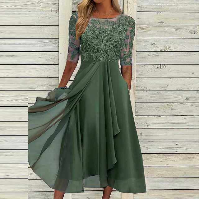Robe verte élégante en dentelle avec manches trois-quarts, jupe fluide, fond en bois clair. Mode féminine, tenue de soirée chic.