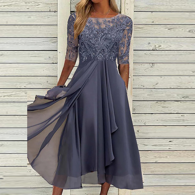 Robe élégante en dentelle grise, manches mi-longues, jupe fluide, fond en bois clair. Mode féminine, tenue de soirée chic, style raffiné.