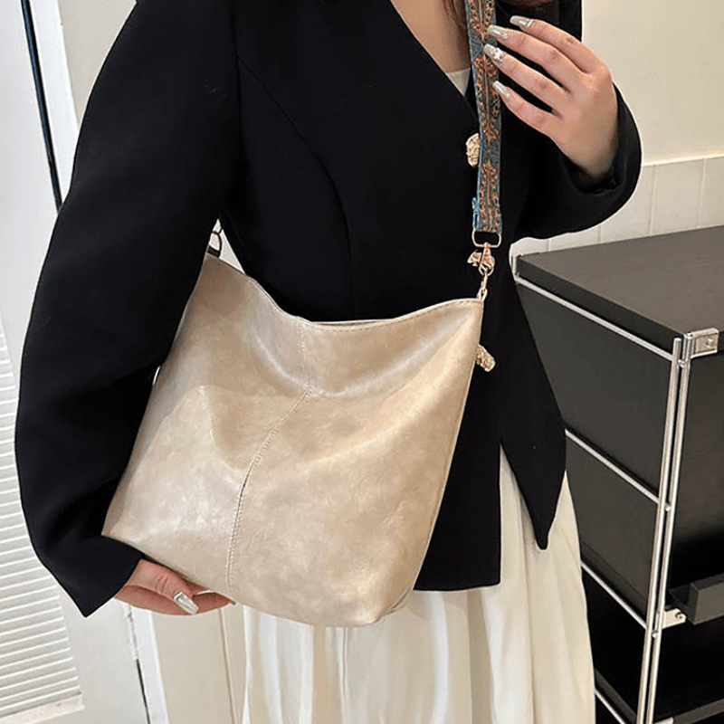 Sac à main en cuir beige porté par une femme en veste noire. Accessoire élégant avec bandoulière décorative, idéal pour la mode urbaine chic.