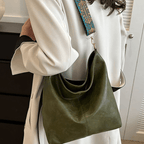 Sac à main vert en cuir avec bandoulière brodée, porté par une femme en manteau blanc. Accessoire de mode élégant et tendance.
