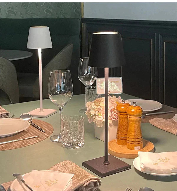 Table élégamment dressée avec lampes modernes, verres à vin, assiettes blanches, serviettes, moulin à poivre et sel, et décoration florale.