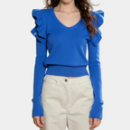 Femme portant un pull bleu à volants avec col en V, manches longues, associé à un pantalon beige. Mode féminine élégante et moderne.