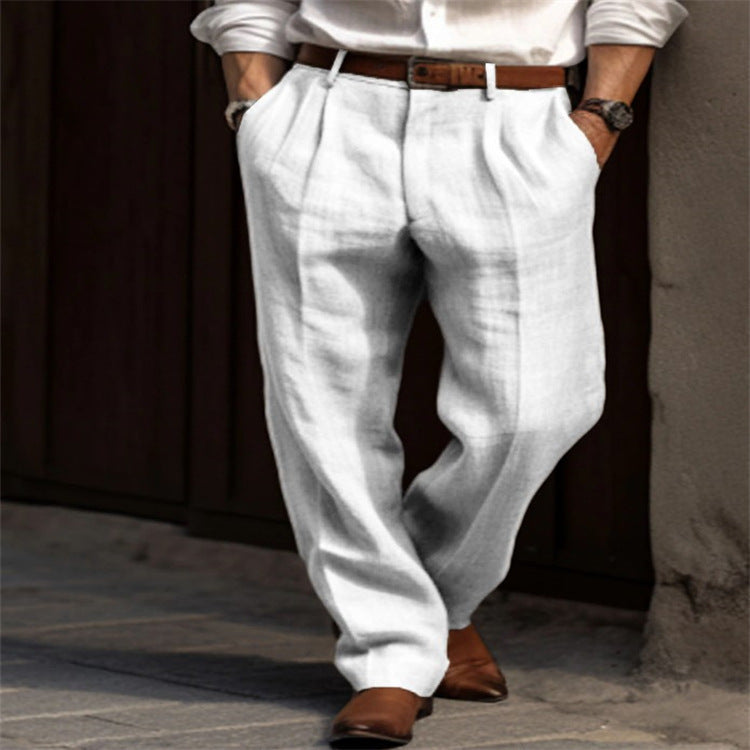 Homme portant un pantalon en lin blanc, chemise blanche et ceinture marron, marchant sur un trottoir. Mode masculine élégante et décontractée.