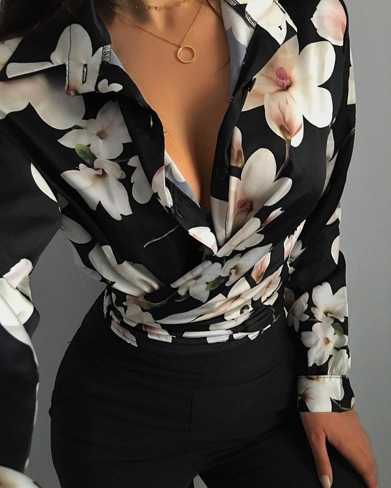 Chemisier noir à fleurs blanches, décolleté en V, porté avec un collier doré et un pantalon noir. Mode féminine élégante et tendance.