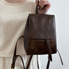 Sac à dos en cuir marron foncé porté par une personne en robe beige. Design élégant, minimaliste, idéal pour mode urbaine et tendance.