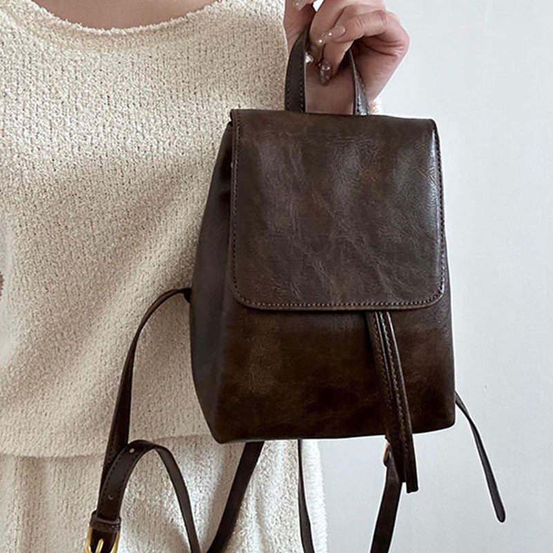 Sac à dos en cuir marron foncé porté par une personne en robe beige. Design élégant, minimaliste, idéal pour mode urbaine et tendance.