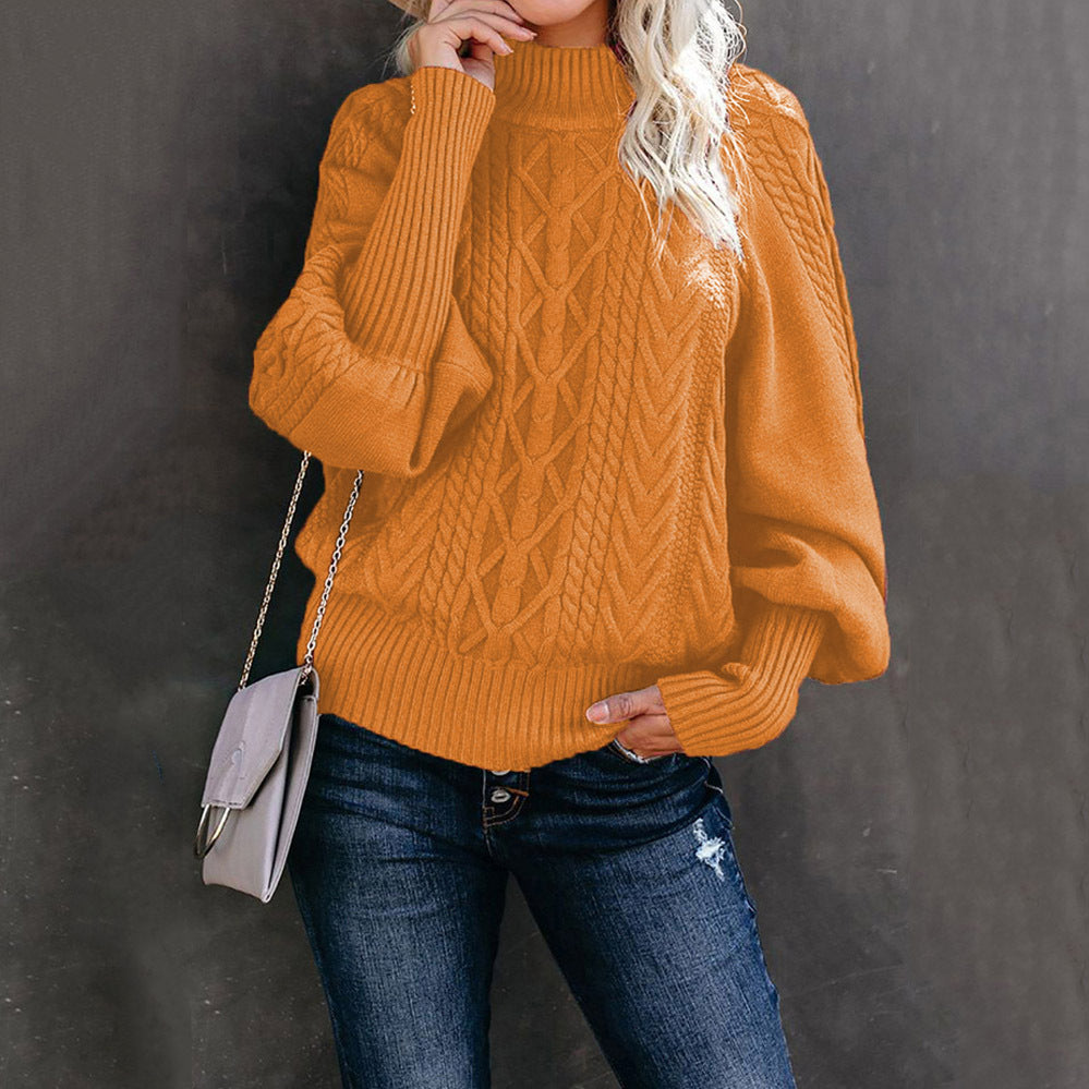 Femme portant un pull en maille orange à col roulé, manches bouffantes, avec un sac à bandoulière gris, posant contre un mur sombre.