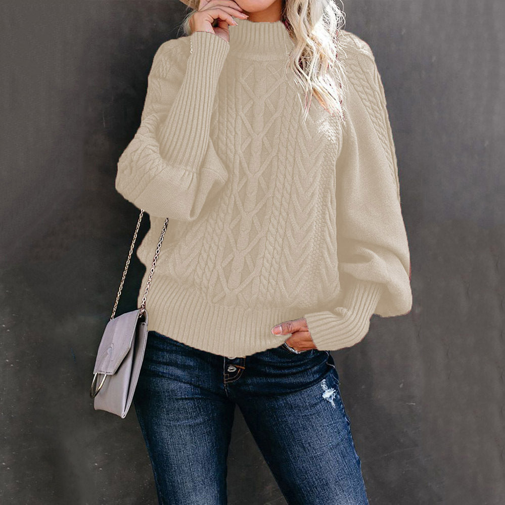 Femme portant un pull en tricot beige à col roulé avec un sac à main gris, posant contre un mur sombre. Mode automne, style décontracté, jeans.