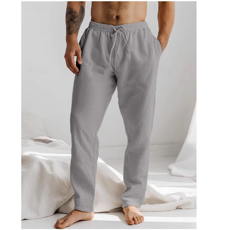 Homme portant un pantalon de pyjama gris en coton, debout dans une chambre lumineuse. Mode détente, confort, vêtements de nuit pour homme.