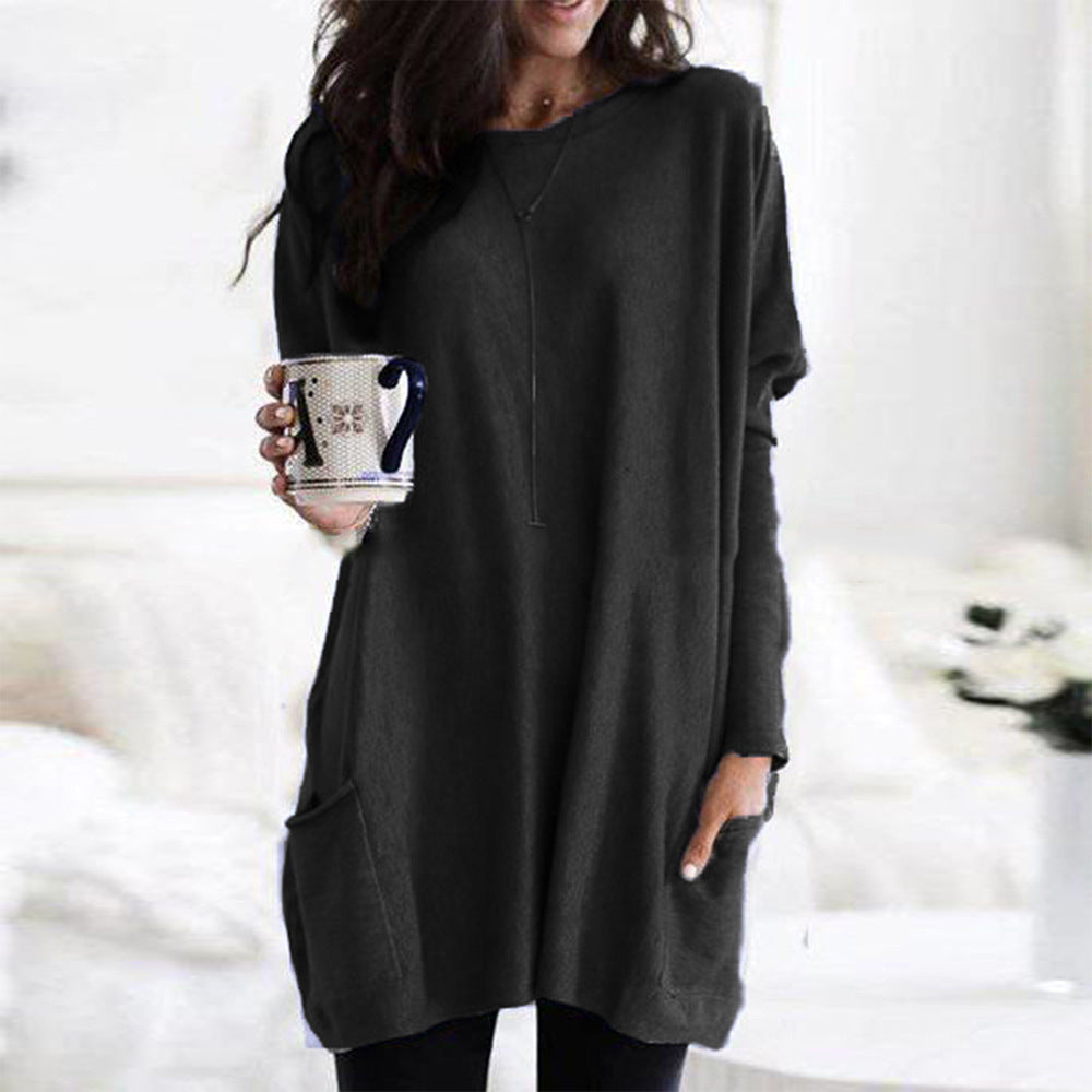 Femme portant une robe pull noire ample, tenant une tasse à motifs. Mode décontractée, style automne-hiver, confort et élégance.