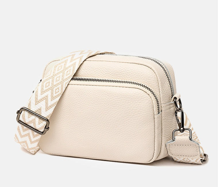 Sac à bandoulière en cuir beige avec sangle à motifs géométriques, fermetures éclair argentées. Accessoire mode tendance pour femme.