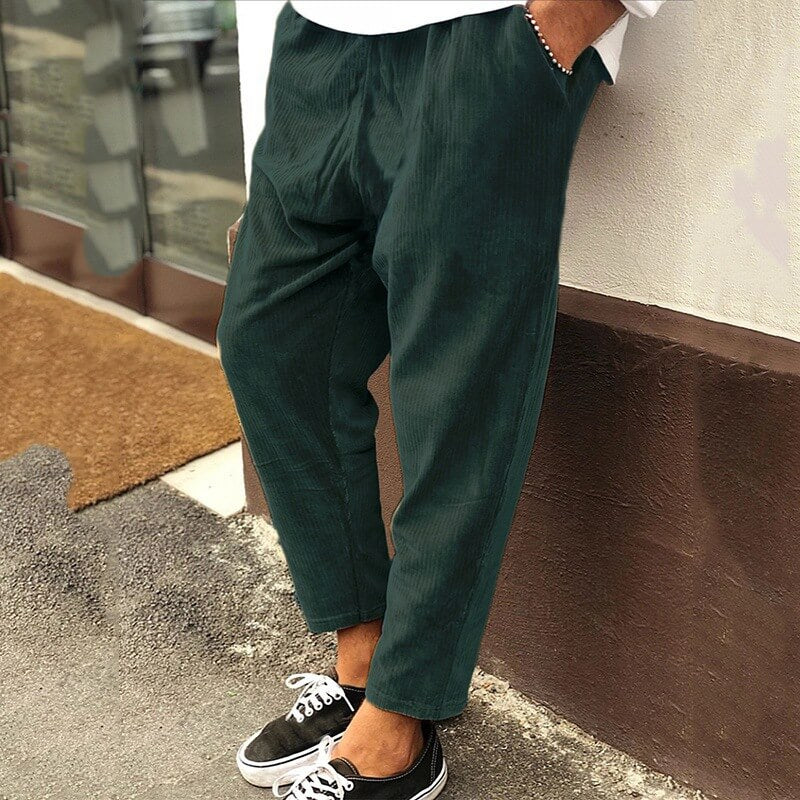 Pantalon vert foncé ample en velours côtelé, style décontracté, porté avec des baskets noires et blanches, mode urbaine moderne pour homme.