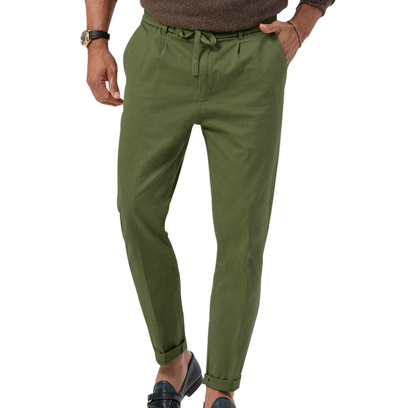 Pantalon vert olive pour homme, coupe ajustée, avec ceinture à cordon, porté avec des mocassins noirs et un pull marron. Mode masculine élégante.