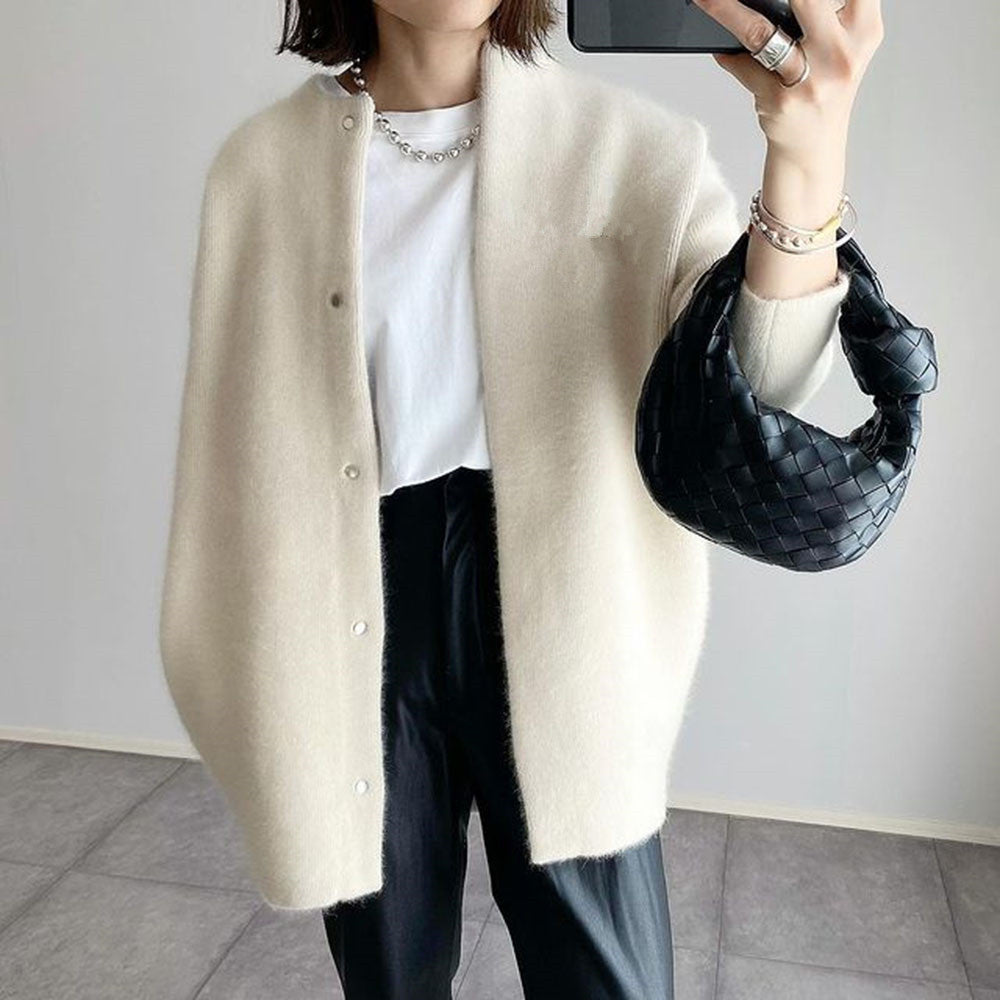 Femme portant un cardigan beige, t-shirt blanc, pantalon noir, sac à main tressé noir, prenant un selfie. Mode élégante et moderne.