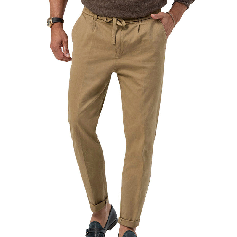 Pantalon chino beige pour homme, coupe ajustée, avec ceinture à nouer, porté avec des mocassins noirs et un pull marron. Mode masculine élégante.