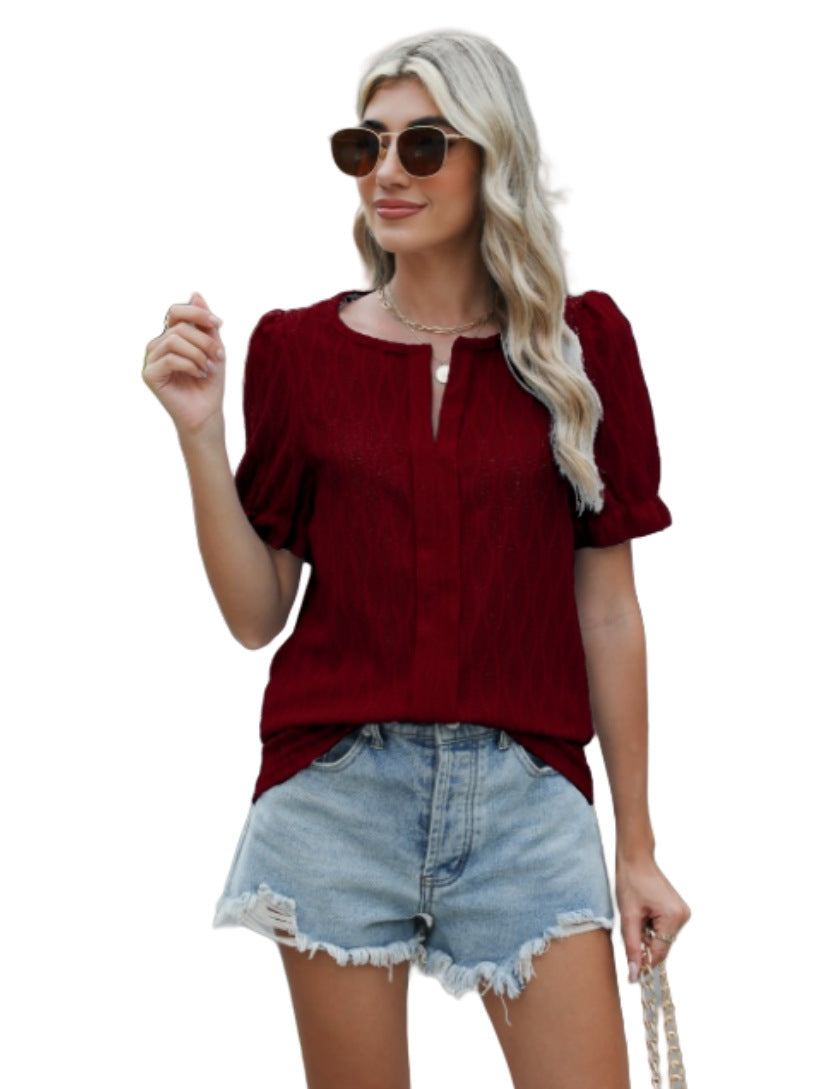 Femme en blouse rouge à manches courtes, lunettes de soleil, cheveux blonds ondulés, portant un short en jean déchiré, fond blanc.