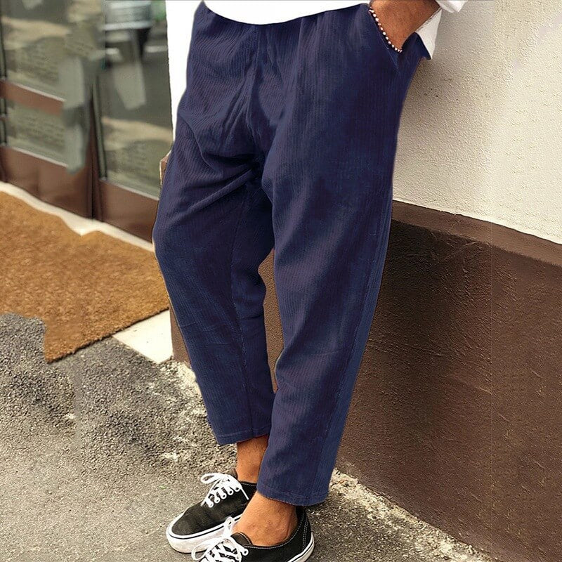 Pantalon ample bleu marine pour homme, style décontracté, porté avec des baskets noires et blanches, devant un mur beige. Mode masculine tendance.
