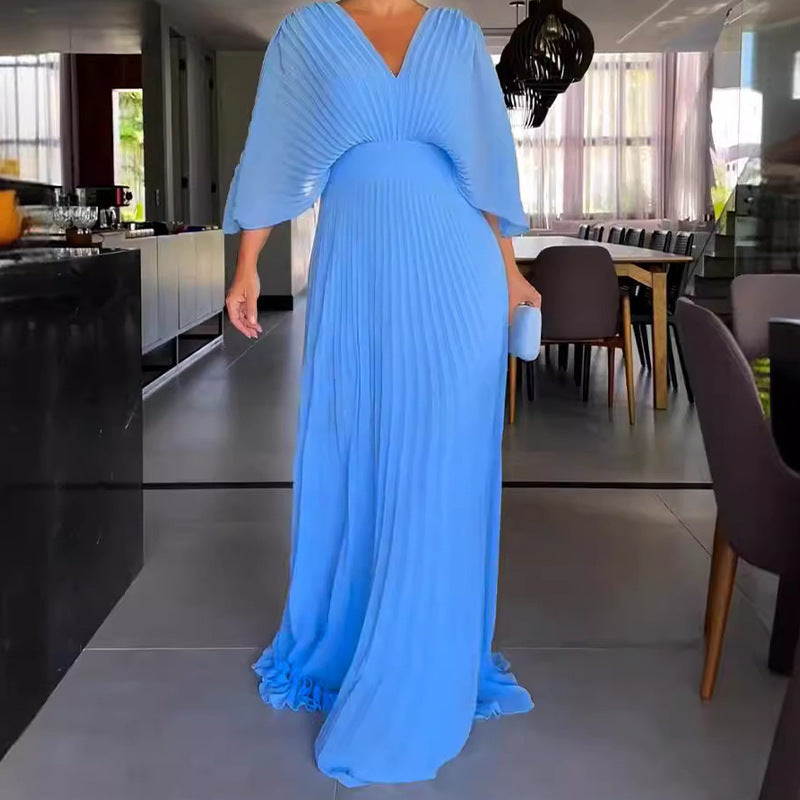Robe longue plissée bleue élégante, manches évasées, portée dans un intérieur moderne. Mode féminine, tenue de soirée chic.
