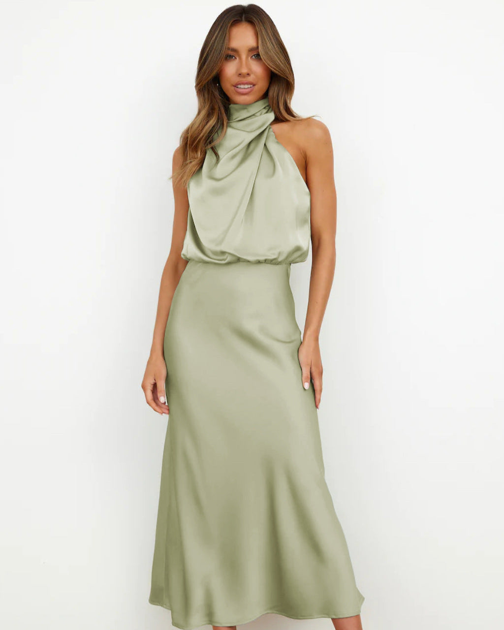 Robe longue en satin vert sauge, col drapé, sans manches, portée par une femme. Mode élégante, tendance, tenue de soirée chic.