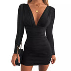 Robe noire moulante à manches longues et décolleté plongeant, accessoirisée d'un sac à main noir avec chaîne dorée et colliers dorés.