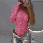 Femme en body asymétrique rose scintillant, pantalon argenté, prenant un selfie. Mode tendance, tenue de soirée glamour, style moderne.