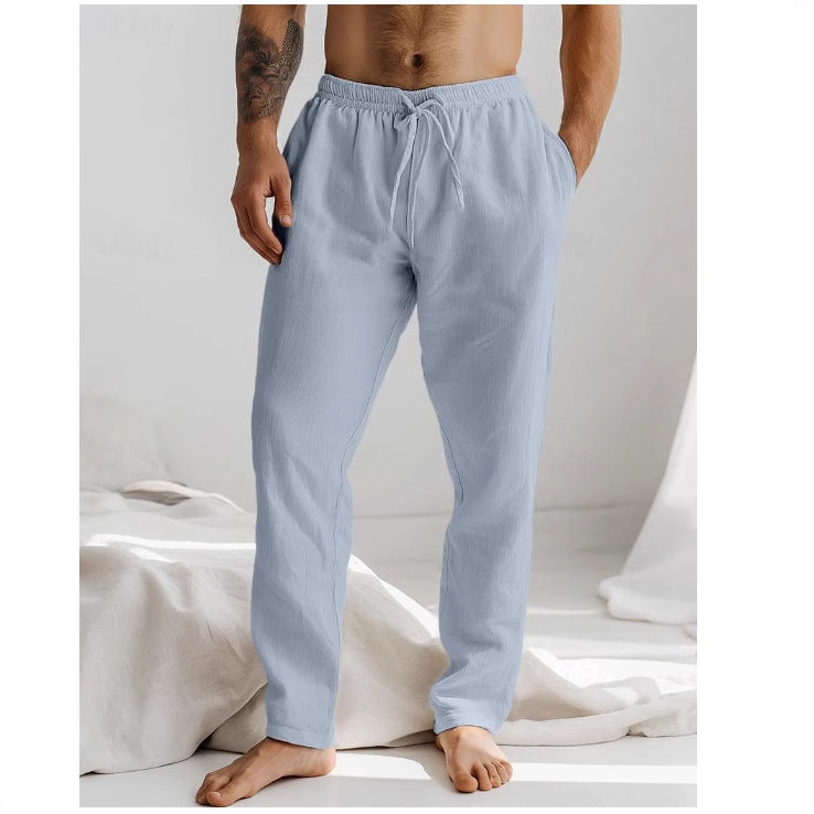 Homme portant un pantalon de pyjama gris clair, debout pieds nus dans une chambre lumineuse. Mode détente, confort, vêtements de nuit pour homme.