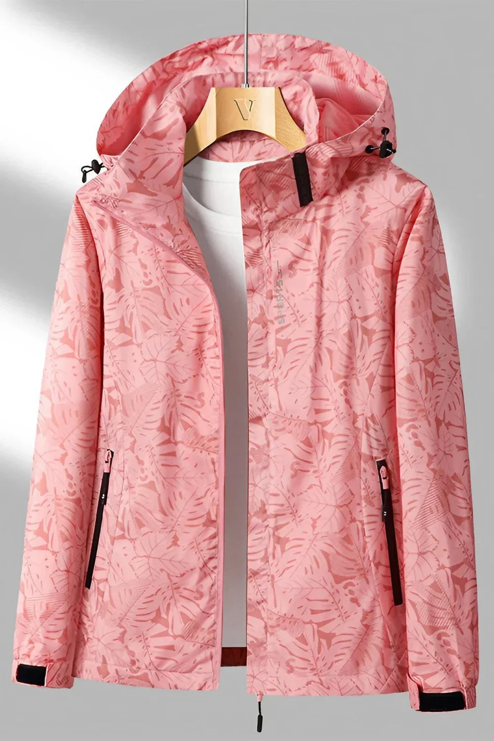 Veste imperméable rose à motifs floraux, capuche ajustable, fermetures éclair noires, accrochée sur un cintre en bois. Mode féminine, vêtements d'extérieur.