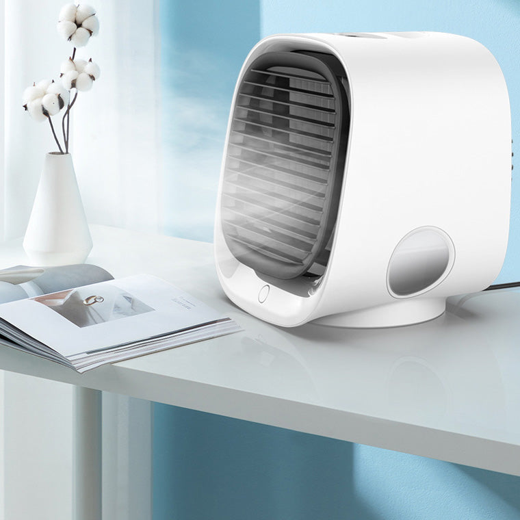 Ventilateur de bureau blanc moderne diffusant de la brume, posé sur une table avec un livre ouvert, dans un intérieur lumineux et minimaliste.