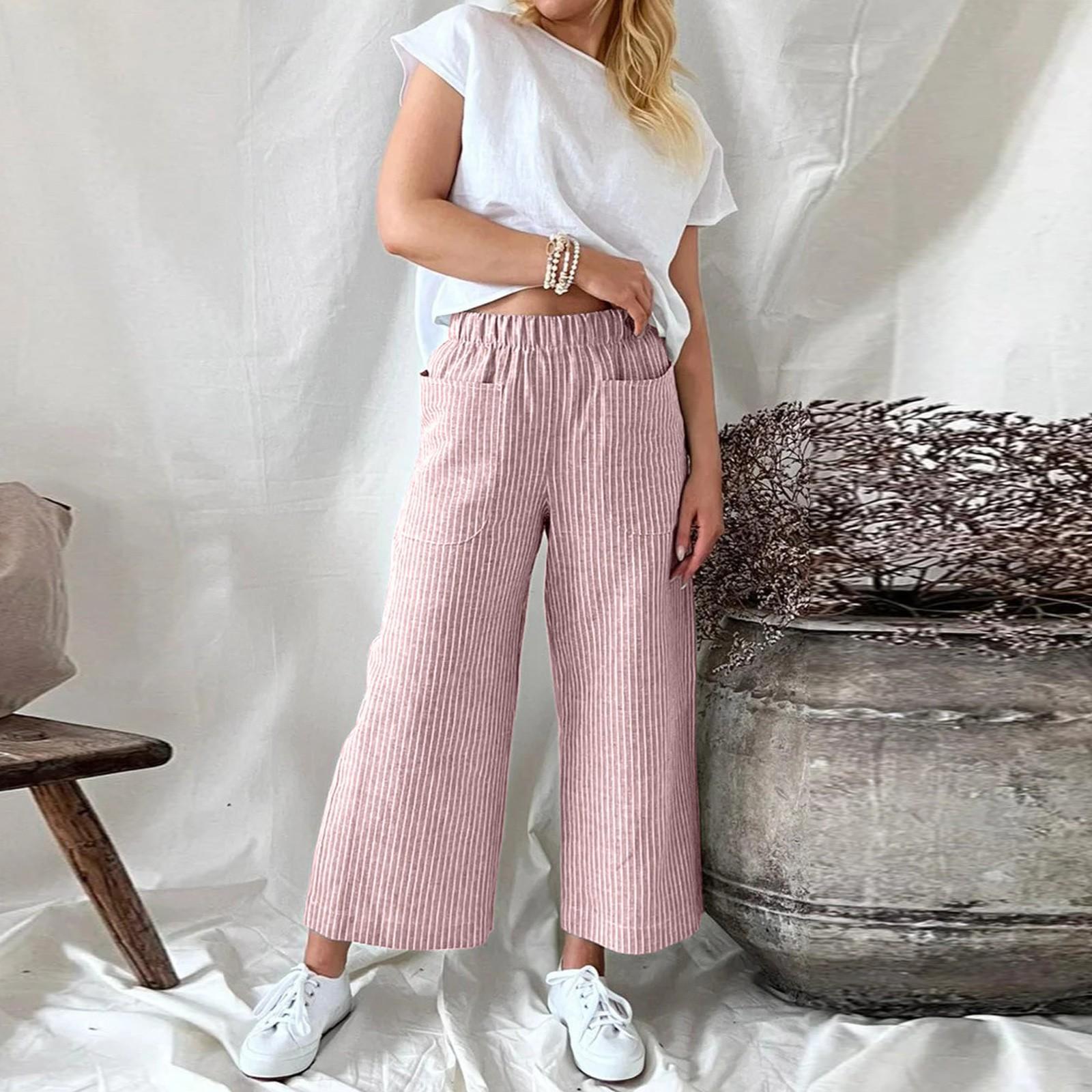 Femme en t-shirt blanc et pantalon rayé rose, posant près d'un grand vase en céramique, style décontracté, mode féminine tendance.