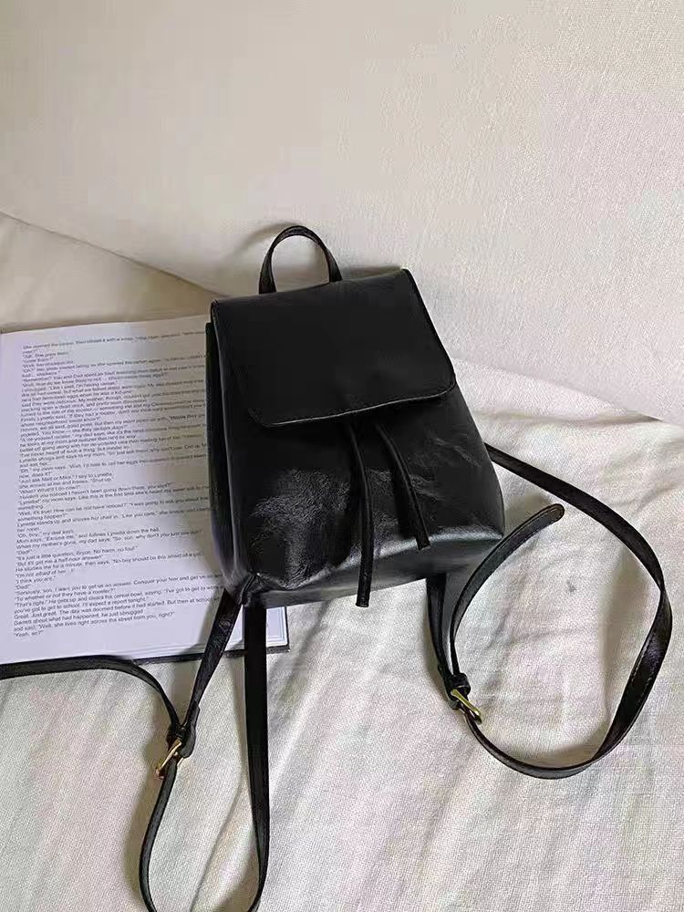 Sac à dos en cuir noir élégant posé sur un lit blanc, à côté d'une feuille de papier imprimée. Accessoire mode tendance et pratique.