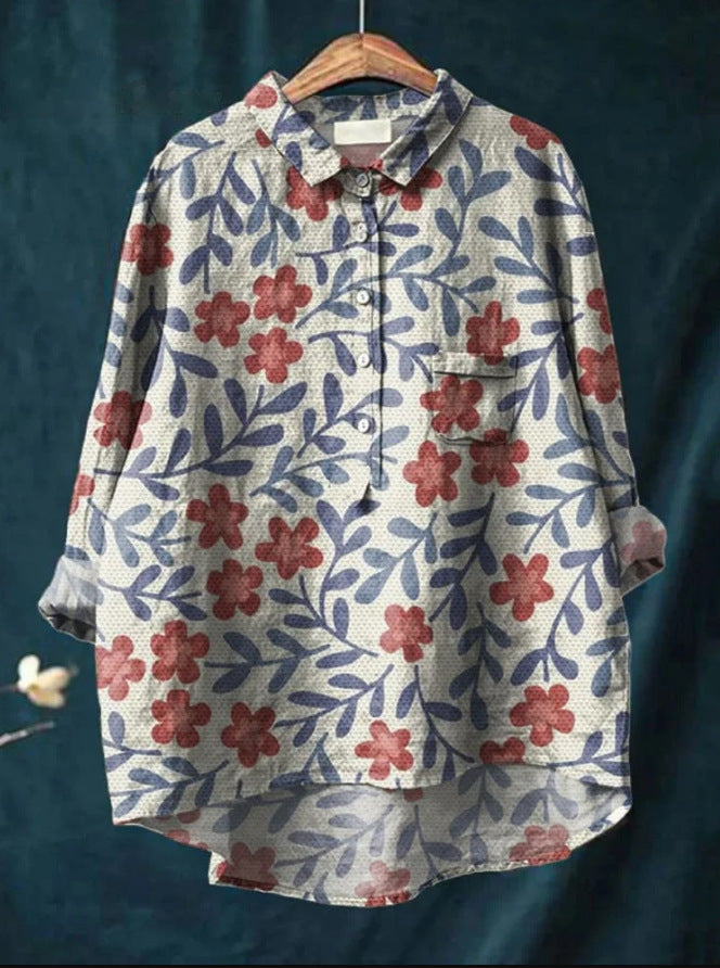 Chemise ample à motifs floraux rouges et bleus sur fond blanc, manches longues, col boutonné, style décontracté, suspendue sur cintre en bois.