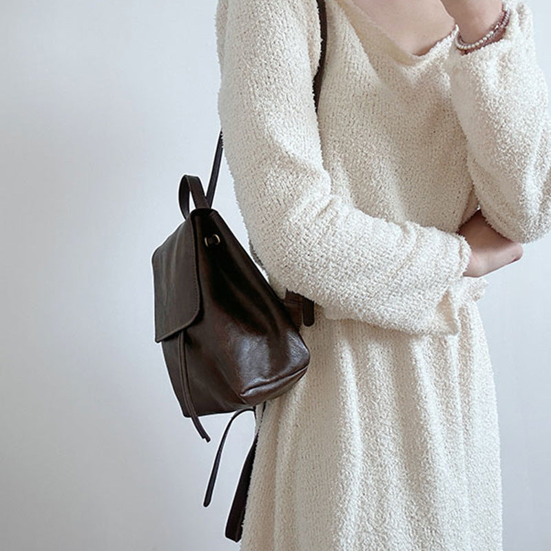 Femme en robe blanche texturée portant un sac à dos en cuir marron foncé. Mode élégante, accessoires tendance, style minimaliste.