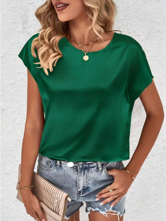 Femme portant un t-shirt vert en satin, short en jean déchiré, collier doré, et tenant une pochette beige. Mode estivale chic et décontractée.